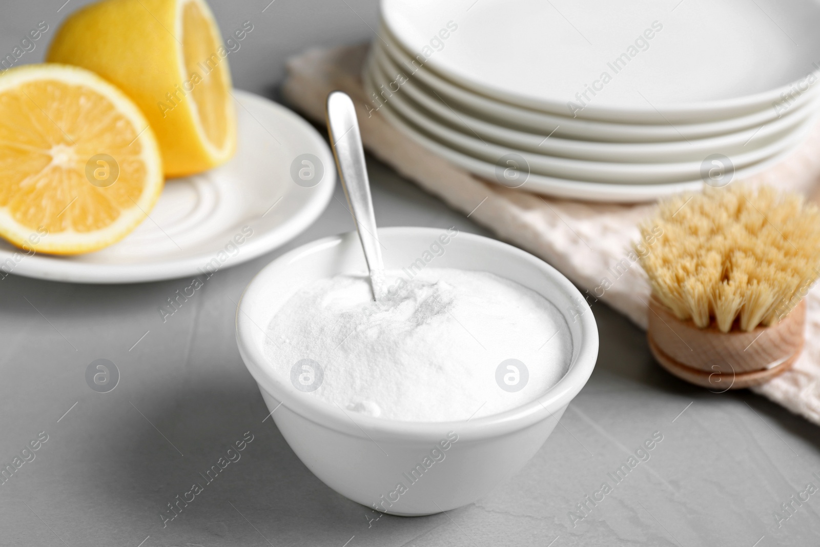 Photo of Bowl of baking soda, brush and lemon on light grey table