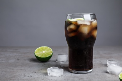 Photo of Refreshing soda drink, ice cubes and lime on table against grey background, space for text