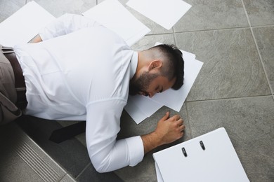 Photo of Unconscious man with scattered folder and papers lying on floor after falling down stairs indoors, top view