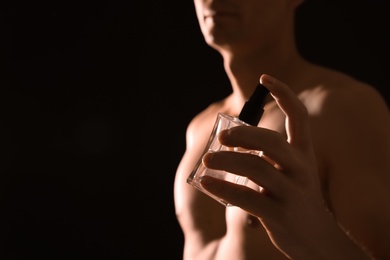 Photo of Young man with perfume bottle on black background, closeup. Space for text