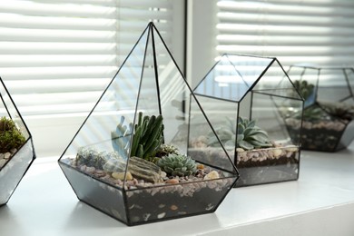 Photo of Glass florarium vases with succulents on white windowsill indoors