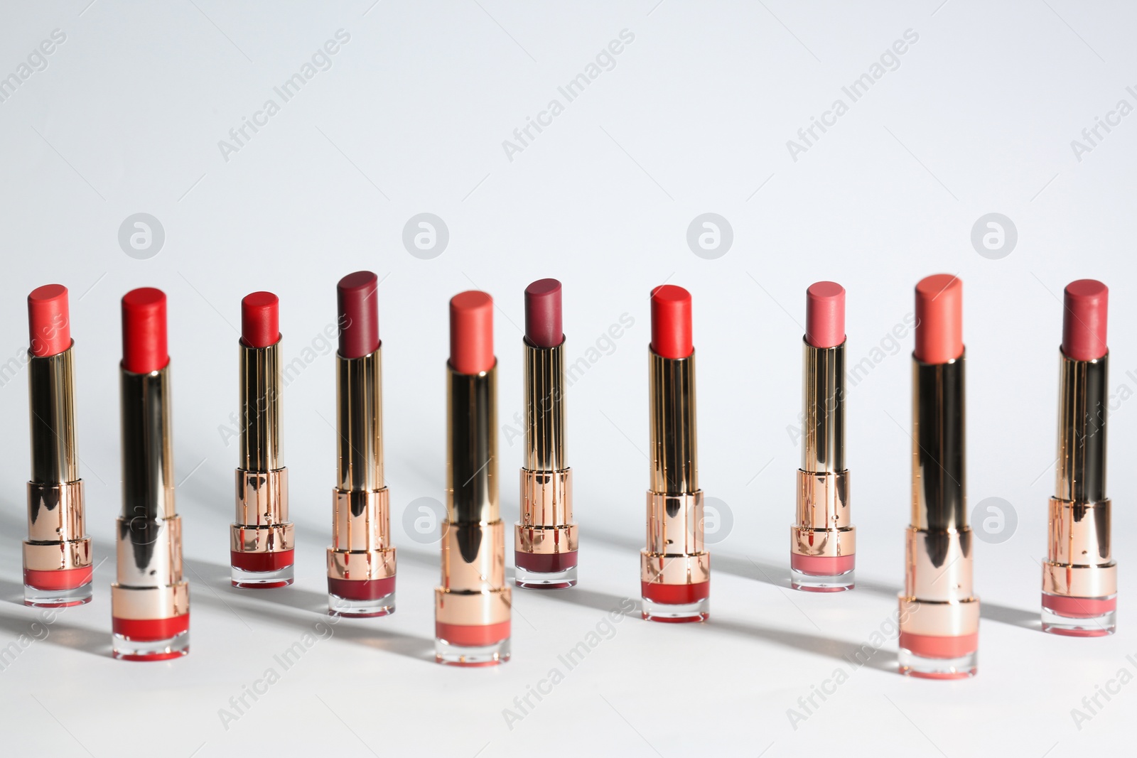 Photo of Set of bright lipsticks in gold tubes on white background
