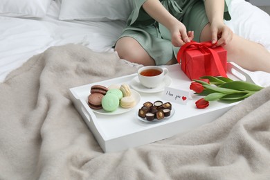 Photo of Tasty breakfast served in bed. Woman with gift box, desserts, tea, flowers and I Love You card at home, closeup