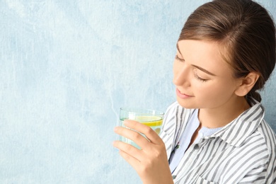 Young woman drinking water with lemon against color background