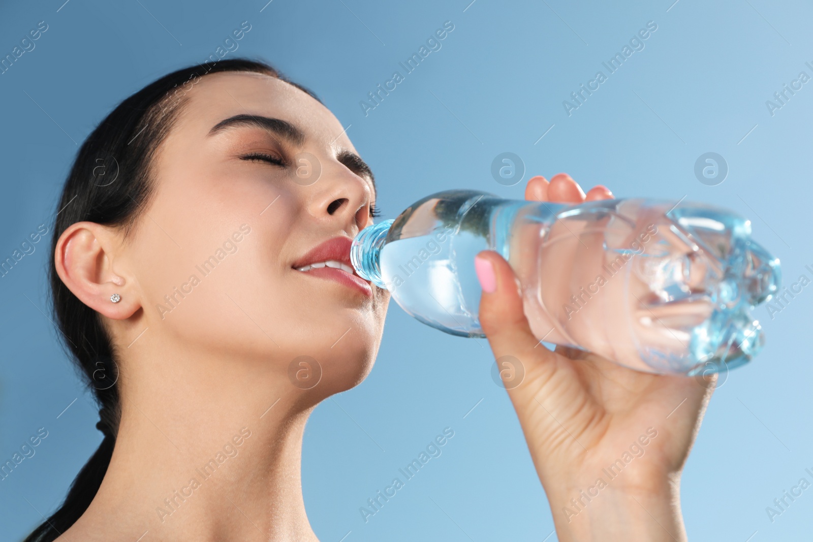 Photo of Beautiful young sportswoman drinking water outdoors, closeup. Refreshing drink