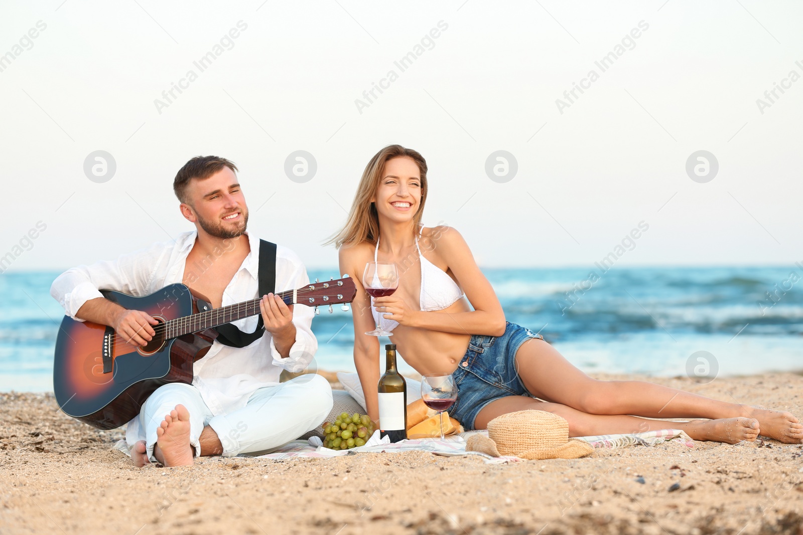 Photo of Young couple with guitar having romantic dinner on beach