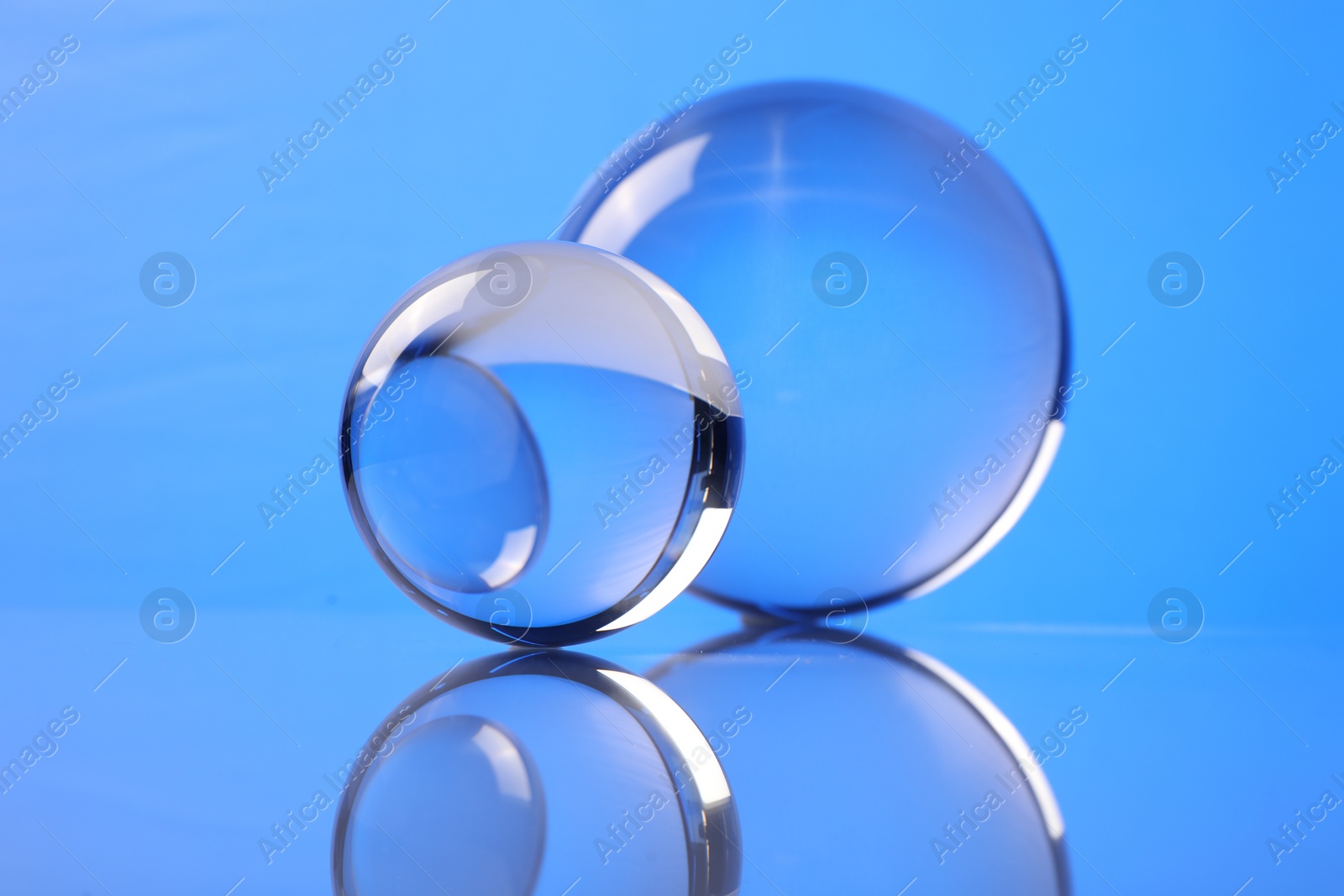 Photo of Transparent glass balls on mirror surface against blue background