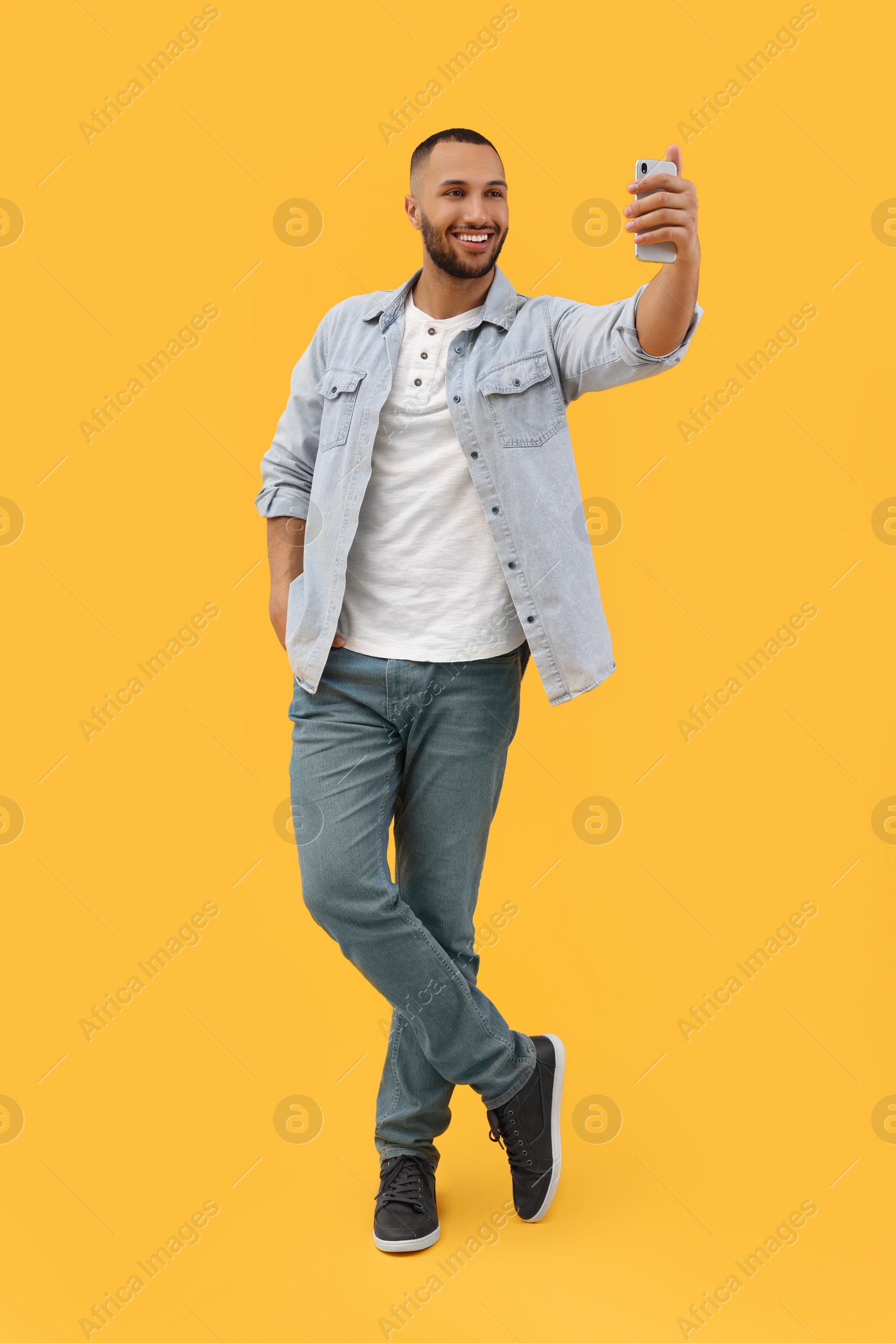 Photo of Smiling young man taking selfie with smartphone on yellow background