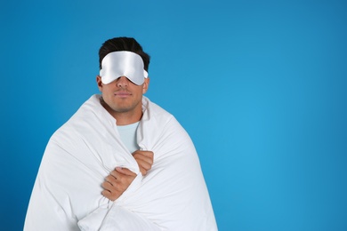 Man wrapped in blanket wearing sleeping mask on blue background. Space for text