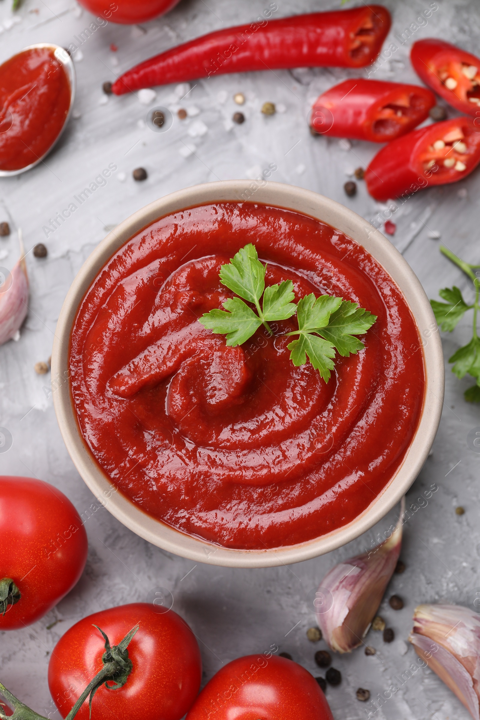 Photo of Flat lay composition with organic ketchup in bowl on grey textured table. Tomato sauce