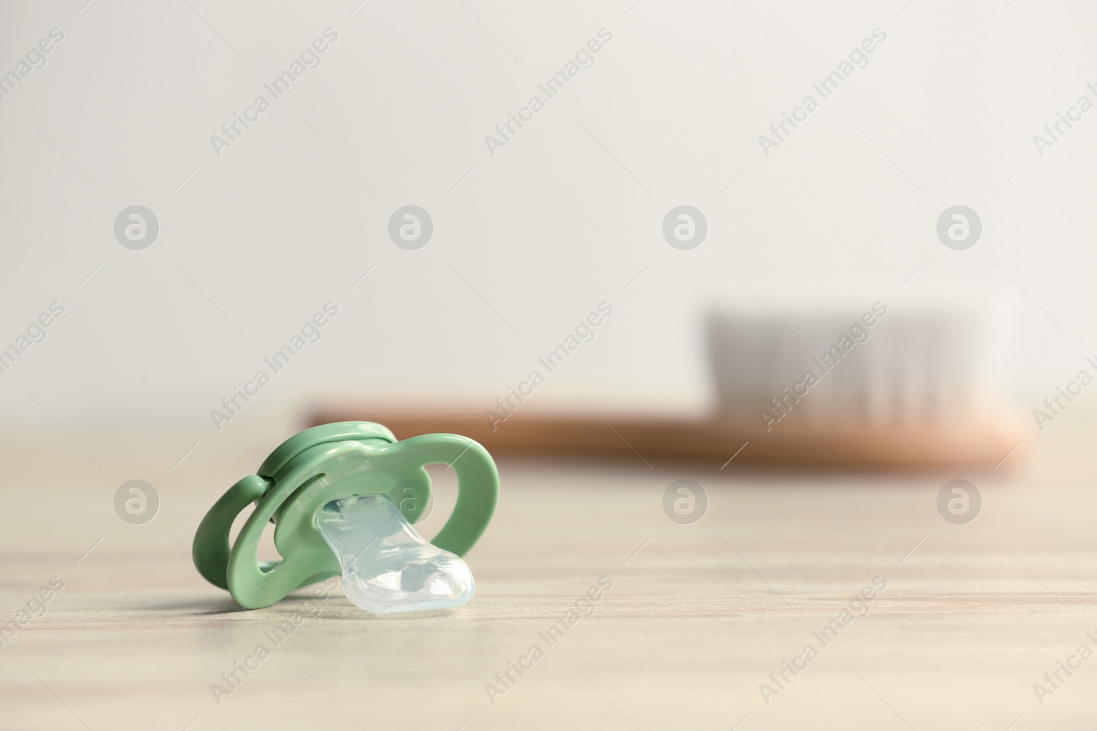 Photo of Baby pacifiers on beige table against blurred background, space for text