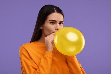 Woman inflating yellow balloon on purple background