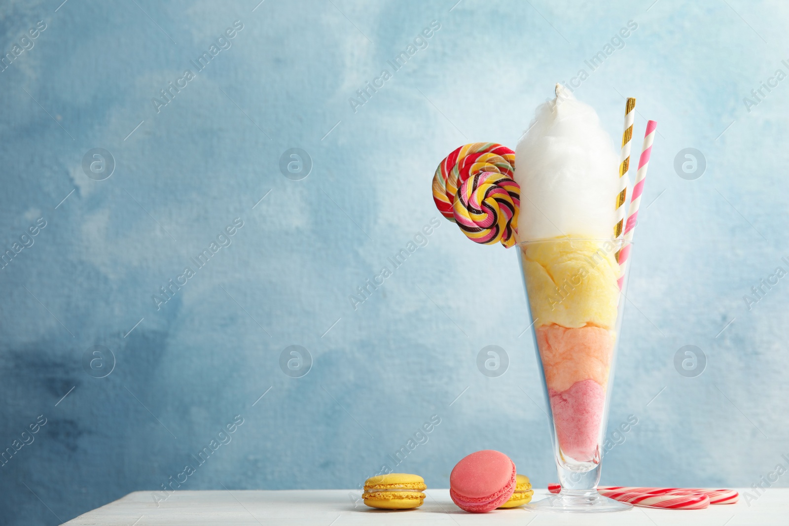 Photo of Yummy cotton candy in glass served with sweets on table. Space for text