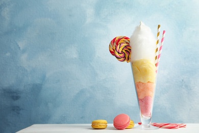 Yummy cotton candy in glass served with sweets on table. Space for text