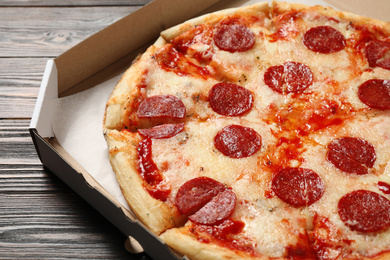 Photo of Hot delicious pepperoni pizza in cardboard box on wooden table, closeup