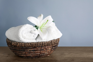 Photo of Fresh towels and lily flower on wooden table, space for text