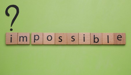 Photo of Motivation concept. Word Impossible and question mark on light green background, flat lay