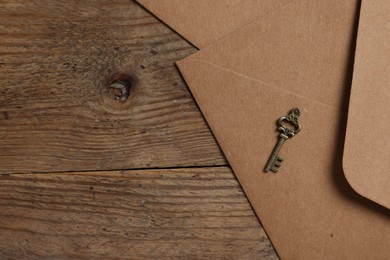 Photo of Paper envelopes and small key on wooden table, flat lay. Space for text