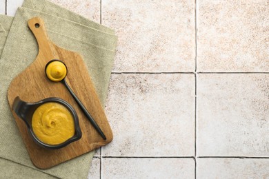 Photo of Tasty mustard sauce on light tiled table, top view. Space for text