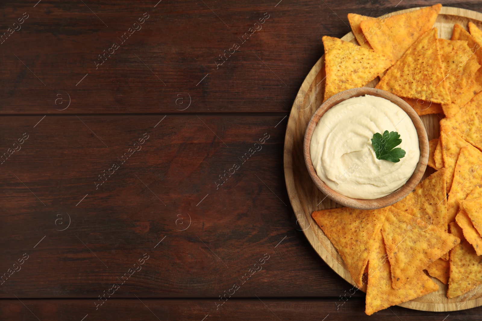 Photo of Delicious hummus with nachos on wooden table, top view. Space for text