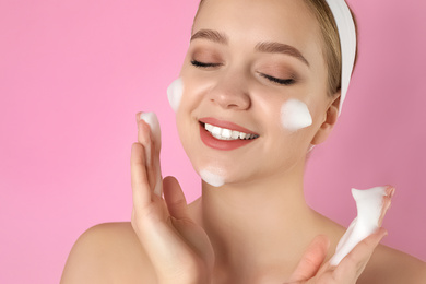 Young woman washing face with cleansing foam on pink background. Cosmetic product