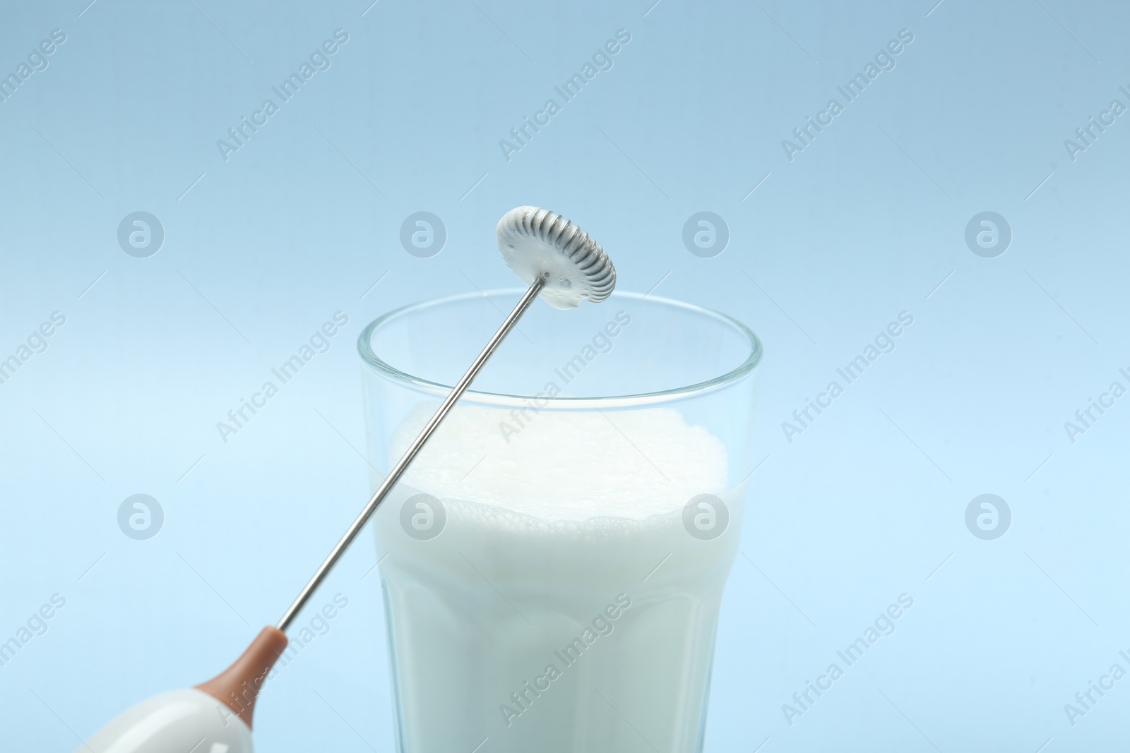 Photo of Mini mixer (milk frother) and whipped milk in glass on light blue background, closeup