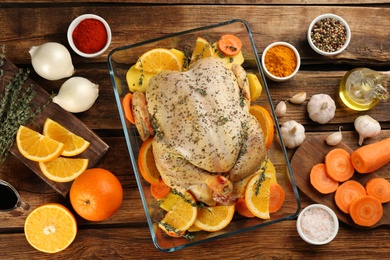 Raw chicken, orange slices and other ingredients on wooden table, flat lay