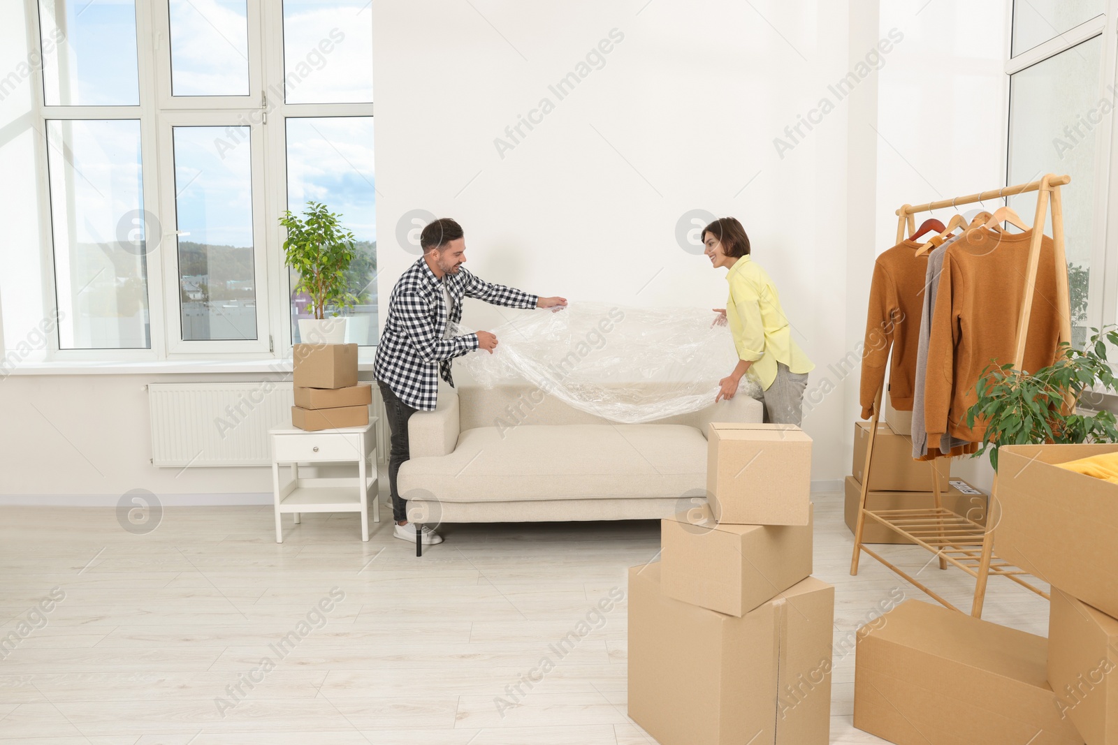 Photo of Happy couple taking plastic film from sofa in new apartment. Moving day