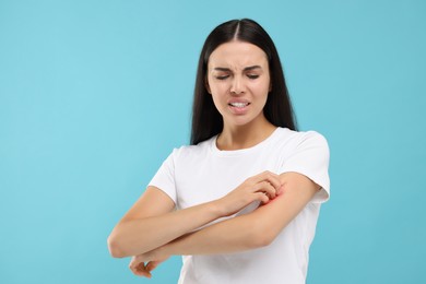 Photo of Suffering from allergy. Young woman scratching her arm on light blue background