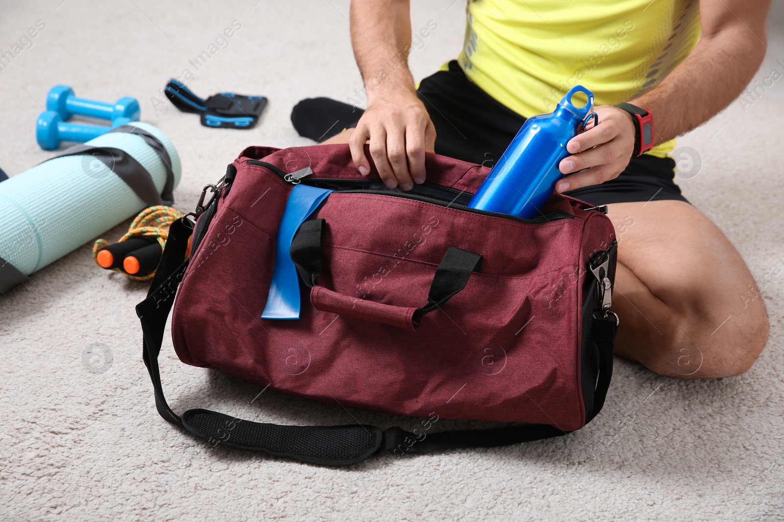 Photo of Man packing sports stuff for training into bag on floor indoors, closeup