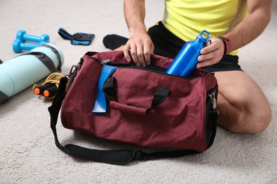 Photo of Man packing sports stuff for training into bag on floor indoors, closeup