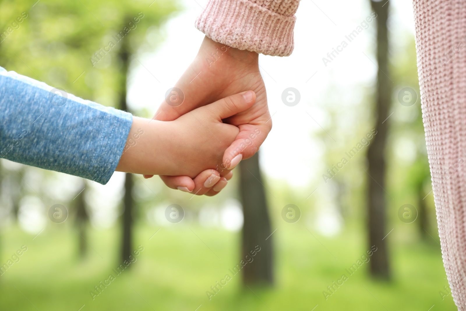 Photo of Little child holding hands with his mother outdoors, closeup. Family time