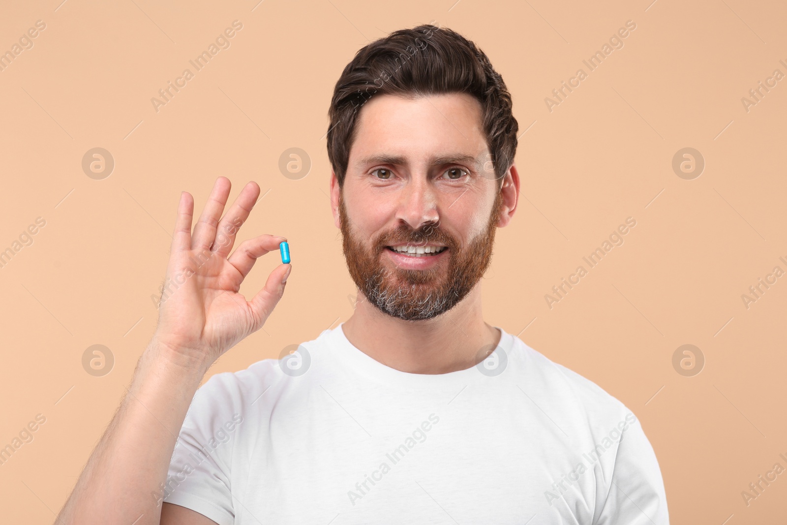 Photo of Handsome man with pill on beige background