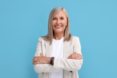 Portrait of beautiful middle aged woman with crossed arms on light blue background