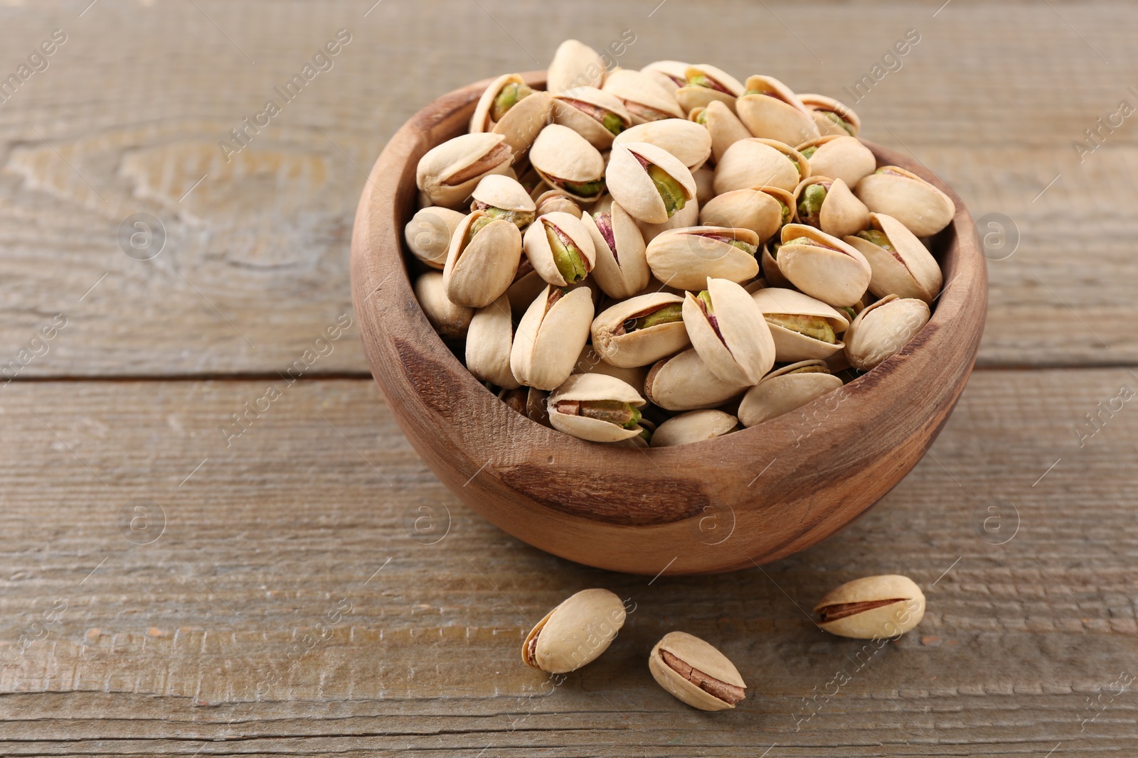 Photo of Delicious pistachios in bowl on wooden table. Space for text