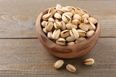 Photo of Delicious pistachios in bowl on wooden table. Space for text