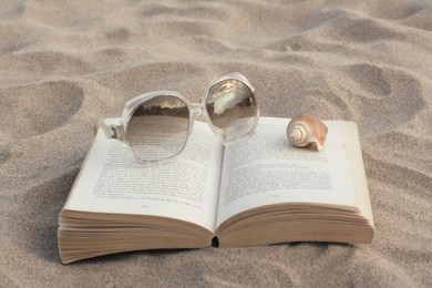Photo of Beautiful sunglasses, book and shell on sand