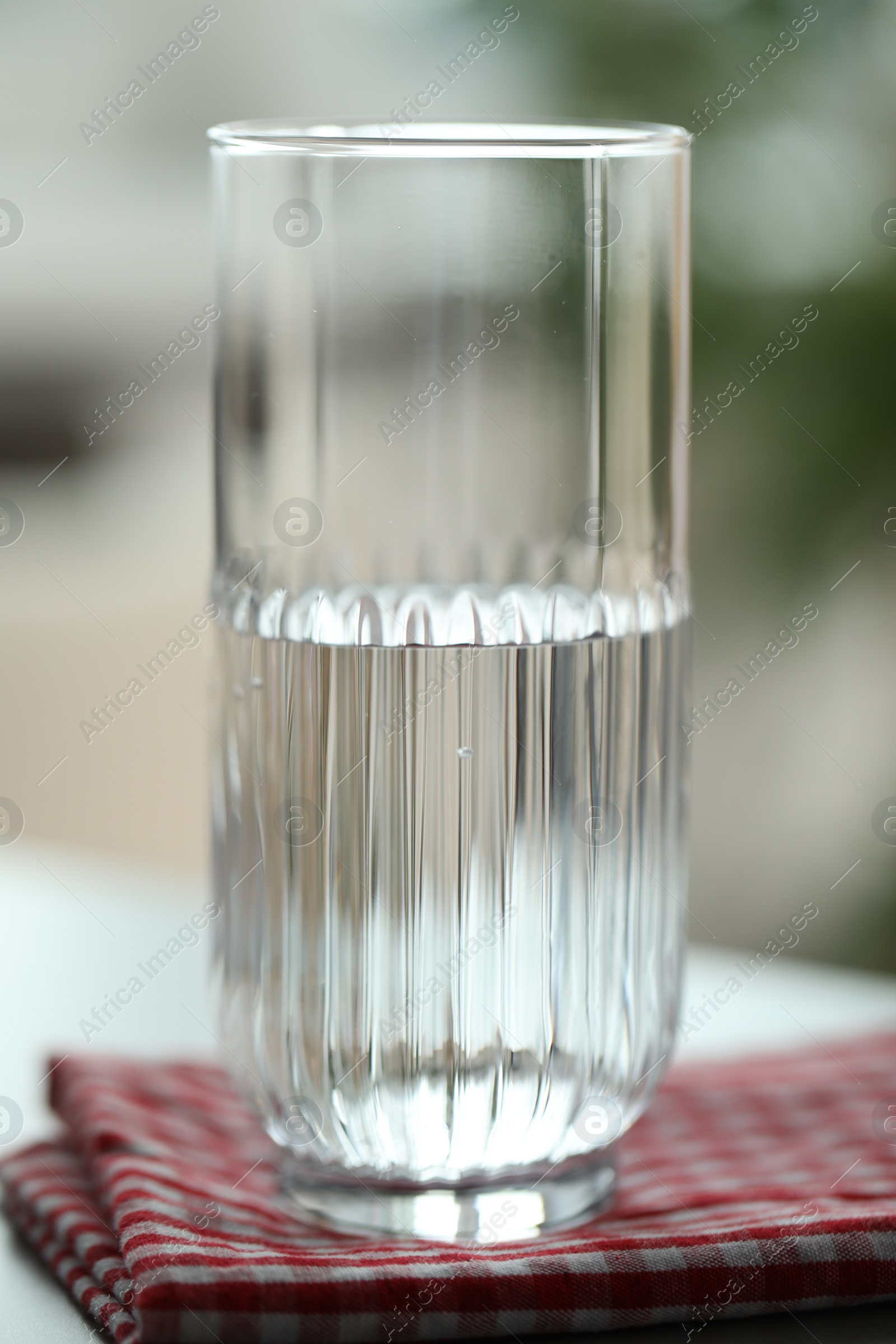 Photo of Glass of pure water on red kitchen towel against blurred background, closeup