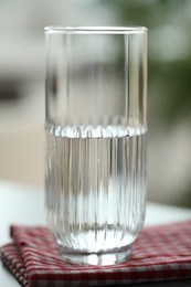 Glass of pure water on red kitchen towel against blurred background, closeup