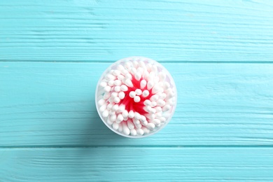 Plastic container with cotton swabs on wooden background, top view