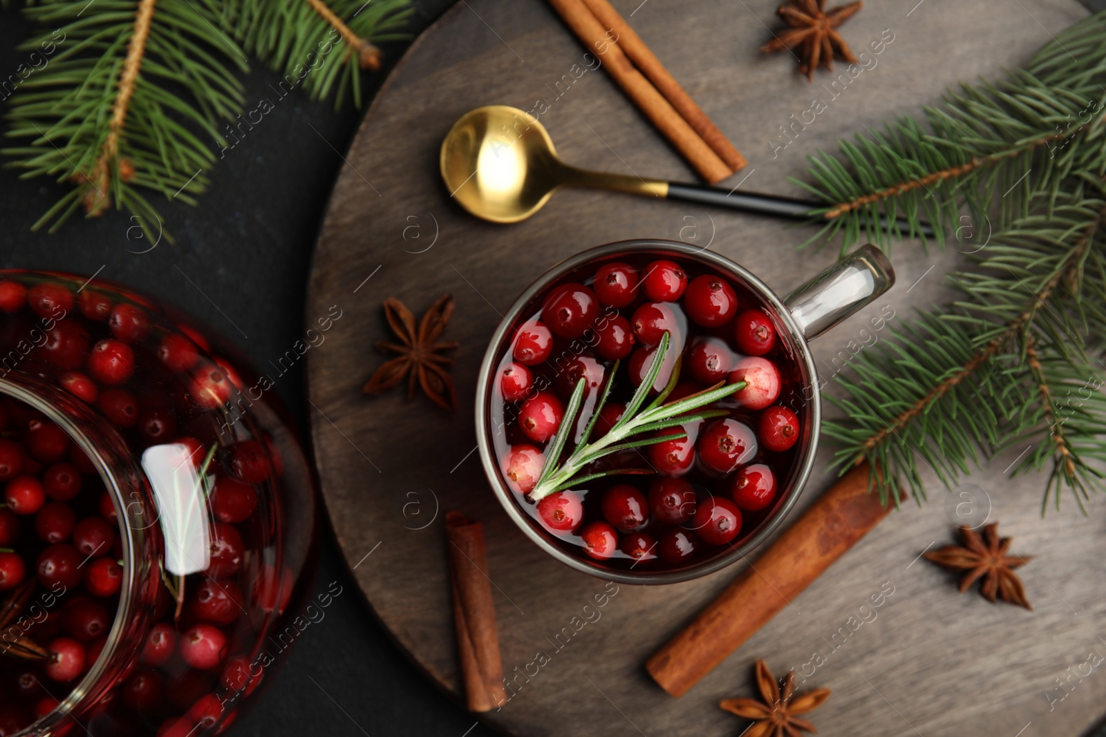 Photo of Tasty hot cranberry tea with rosemary, anise and cinnamon on black table, flat lay