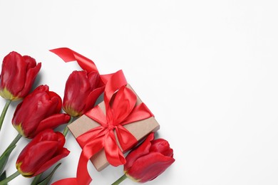 Beautiful gift box and red tulip flowers on white background, flat lay. Space for text