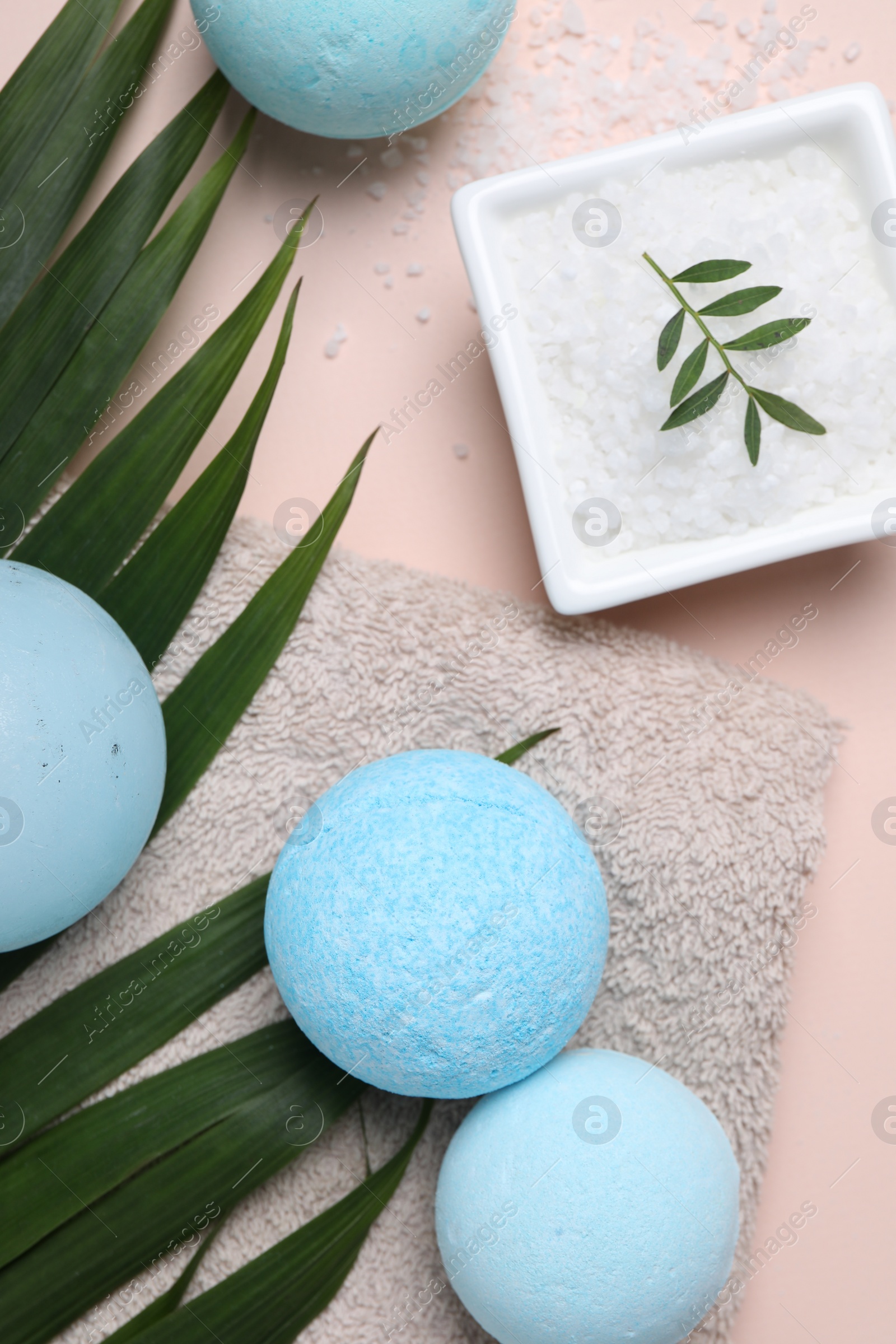 Photo of Bath bombs, green leaf, sea salt and towel on beige background, flat lay