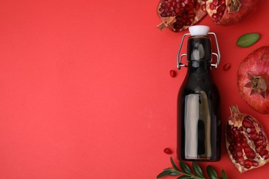 Photo of Tasty pomegranate sauce in bottle, leaves and fruits on red background, flat lay. Space for text