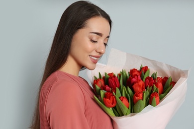 Happy woman with red tulip bouquet on light grey background. 8th of March celebration