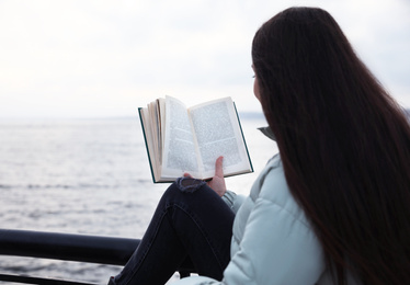 Photo of Woman reading book near river on cloudy day