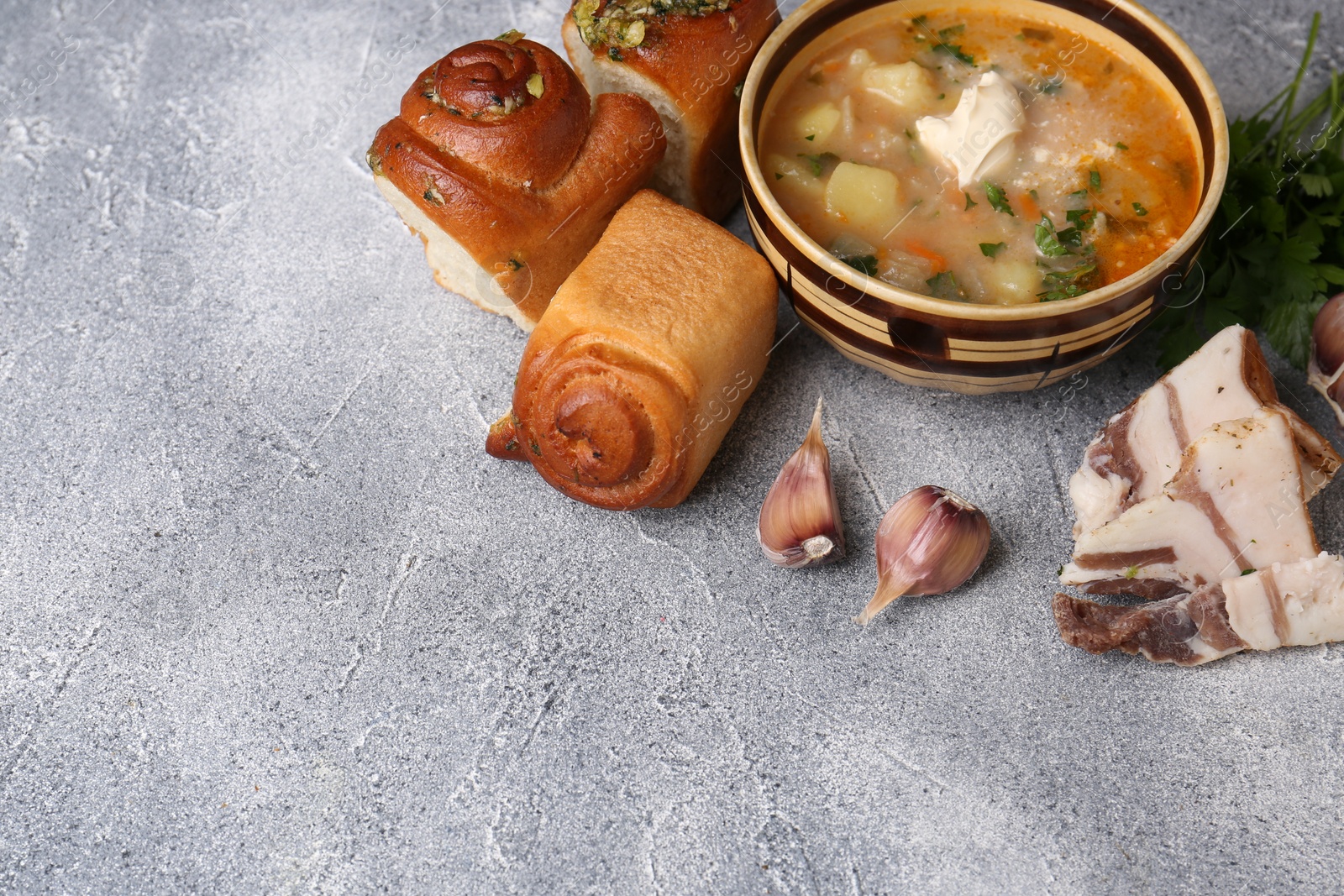 Photo of Delicious borsch served with pampushky and salo on grey textured table, space for text. Traditional Ukrainian cuisine