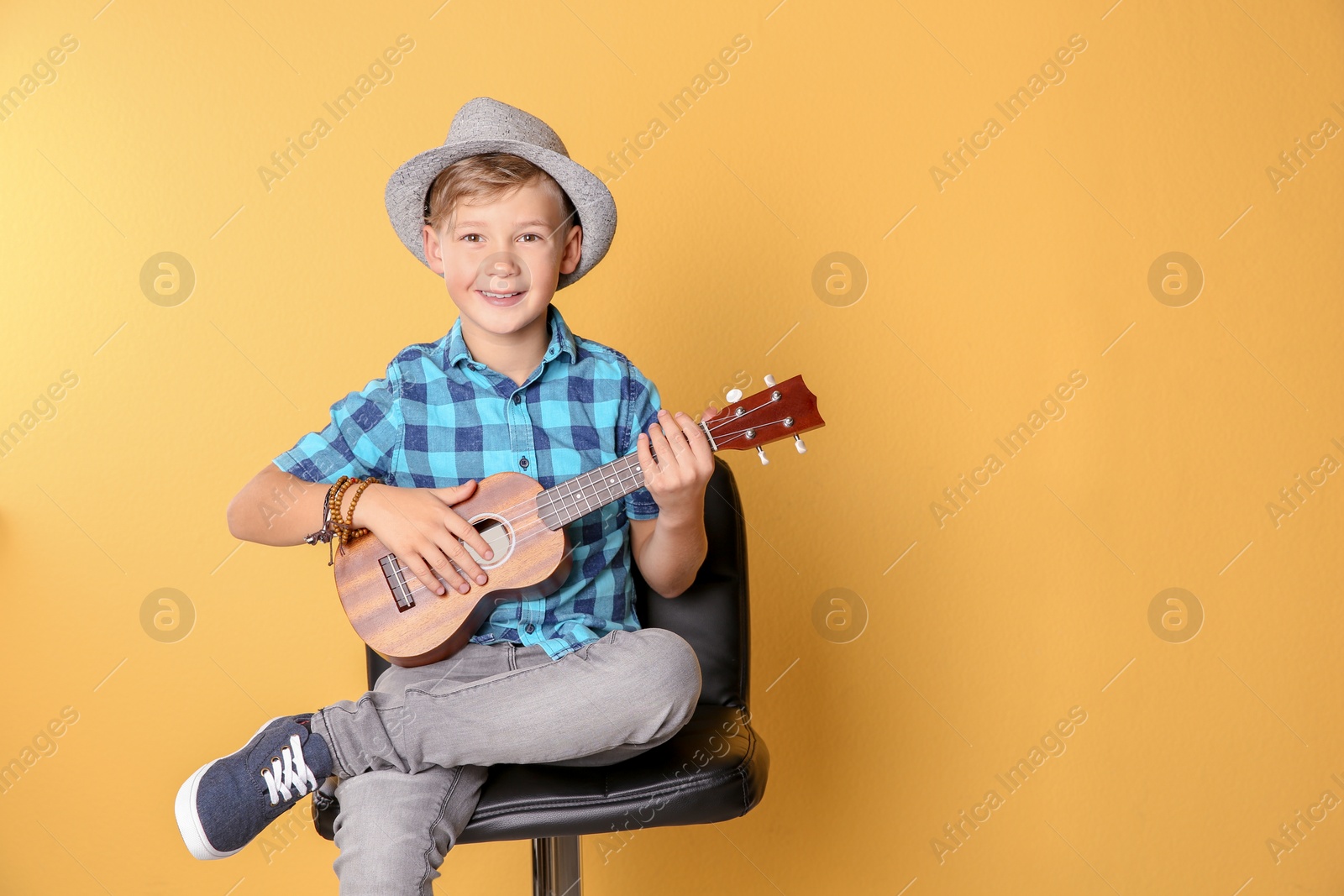 Photo of Little boy sitting on chair and playing guitar against color background. Space for text