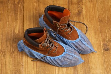 Men`s boots in blue shoe covers on wooden floor, above view