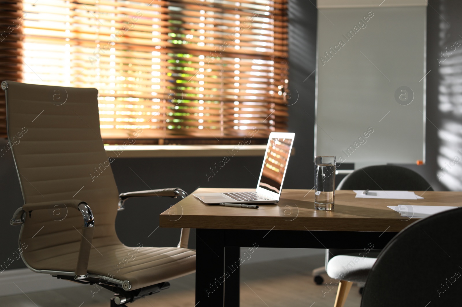 Photo of Laptop and glass of water on wooden table in modern office